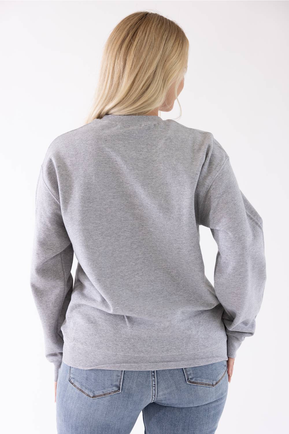 A woman viewed from the back wearing a light gray heather crewneck sweatshirt and blue jeans against a plain white background.