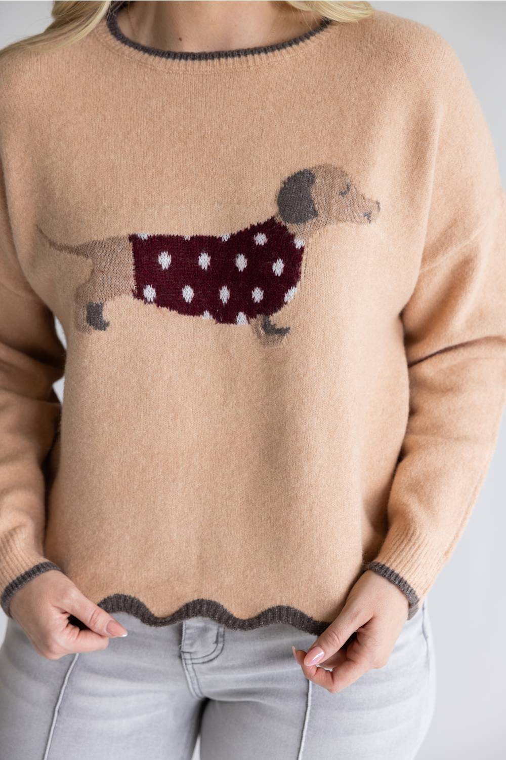 A woman wearing a beige knit sweater with a dachshund graphic wearing a burgundy sweater with white polka dots, paired with light gray jeans.