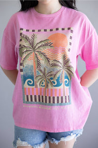 Person wearing a pink t-shirt with a palm tree and sunset design.