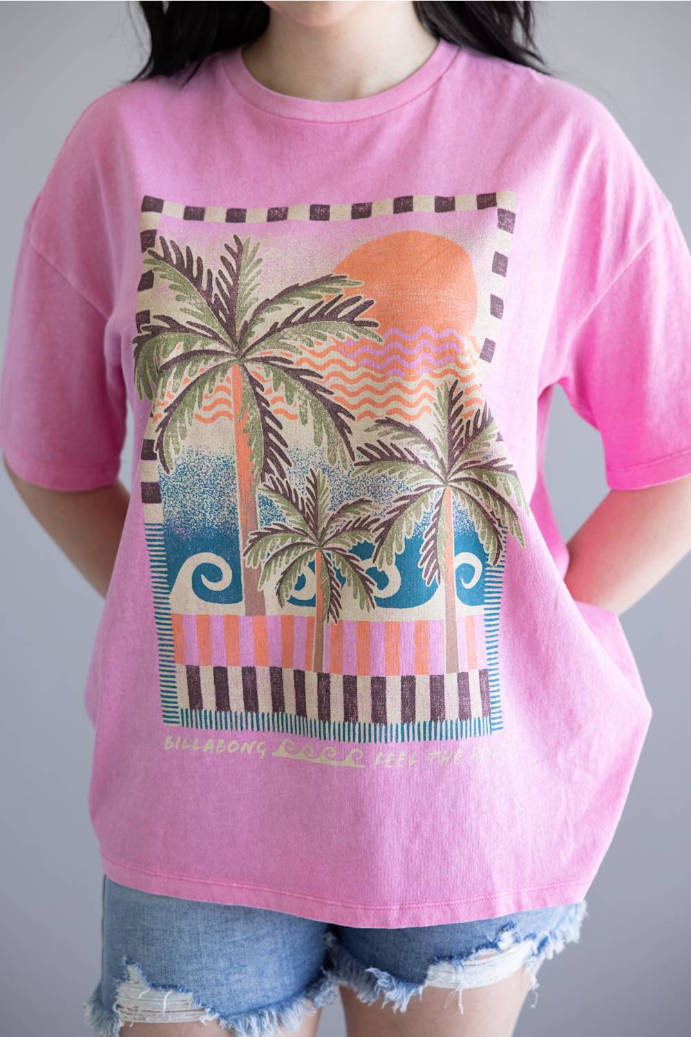 Person wearing a pink t-shirt with a palm tree and sunset design.