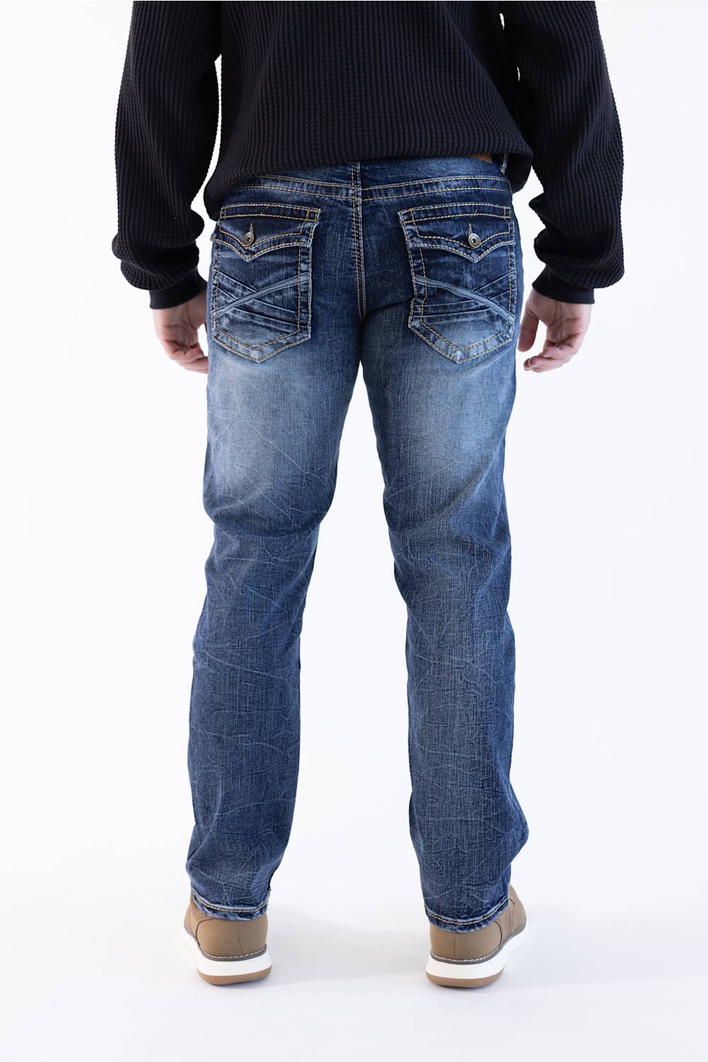 Rear view of a person wearing blue denim jeans with a black ribbed sweater and tan shoes, standing against a plain white studio background.