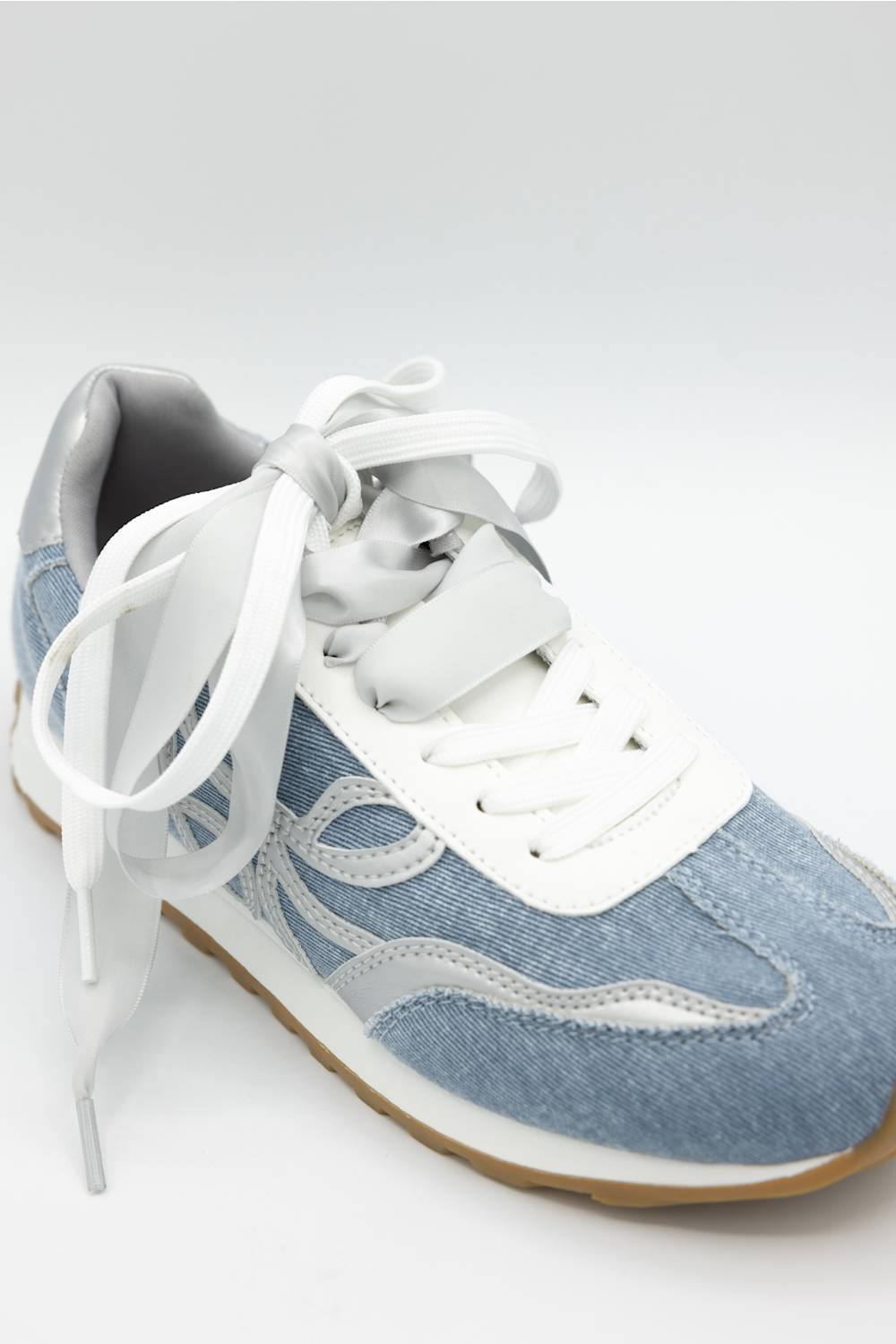 A light blue denim sneaker with white laces, white side panels, and a gum brown sole, photographed on a light gray background.