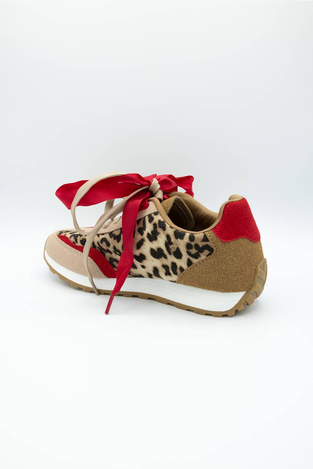 A low-top sneaker featuring a beige and black leopard print pattern on the side, beige suede-like panels on the toe and heel, a red fabric heel tab, and red ribbon laces tied in a bow, shown against a plain white background.