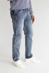 A person wearing light-wash blue denim jeans with white sneakers and a lavender ribbed sweater, shown from the waist down against a plain light gray studio background.