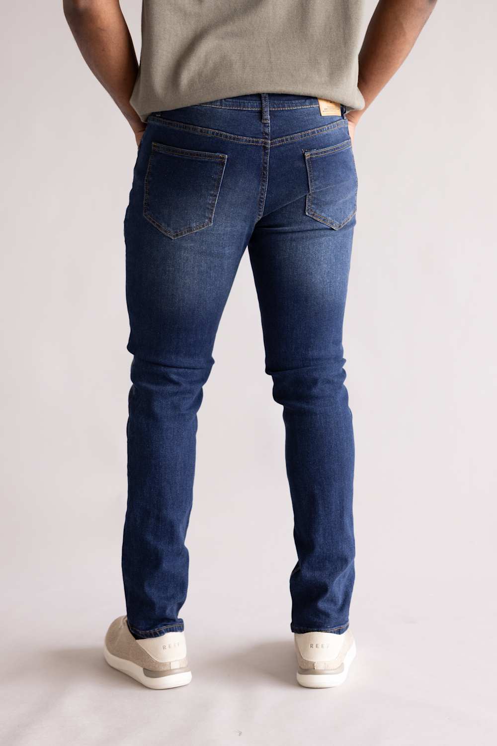 Person wearing blue jeans and a light-colored shirt on a plain background, showing two back pockets. The blue jeans are named Weatherproof Vintage Slim Jeans for Men in Silt Blue.