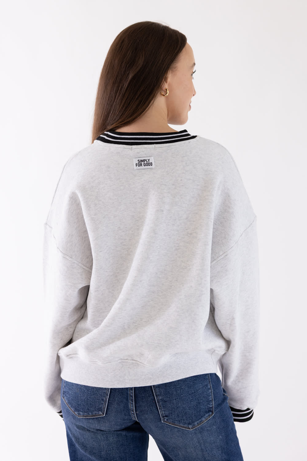 A woman shown from the back wearing a light gray heather crewneck sweatshirt with black and white striped ribbed collar and cuffs, paired with blue jeans, against a plain white background.