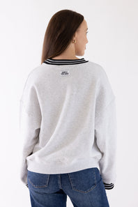 A woman shown from the back wearing a light gray heather crewneck sweatshirt with black and white striped ribbed collar and cuffs, paired with blue jeans, against a plain white background.