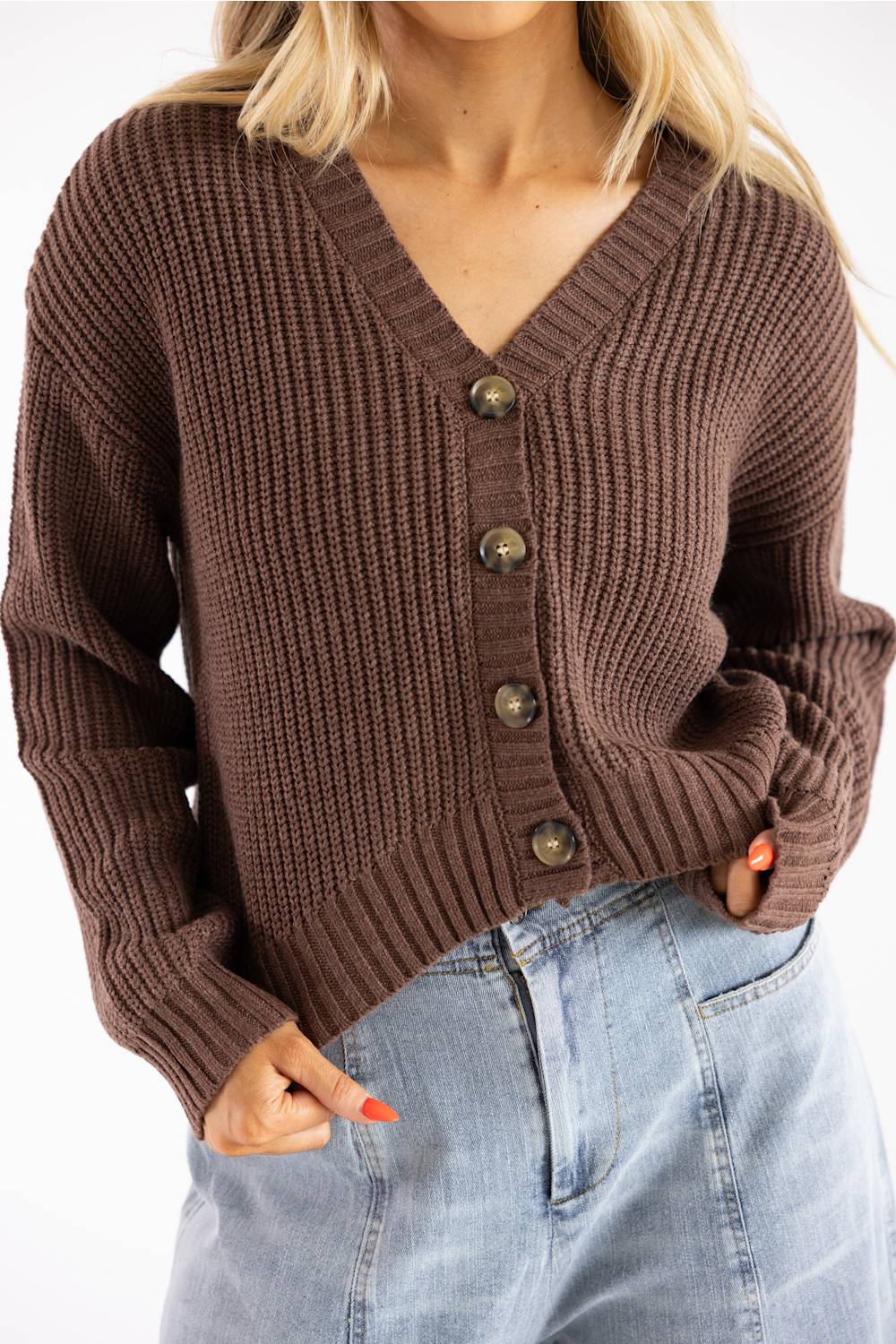 Close-up of a woman wearing a dark brown, V-neck, ribbed button-down cardigan paired with light-wash high-waisted denim jeans, shown from the chest to hips.
