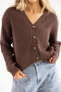 Close-up of a woman wearing a dark brown, V-neck, ribbed button-down cardigan paired with light-wash high-waisted denim jeans, shown from the chest to hips.
