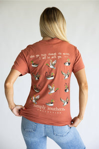 A terracotta-colored short-sleeve t-shirt shown from the back, featuring a graphic print of multiple flying mallards with handwritten-style text above and below. The brand 'simply southern.