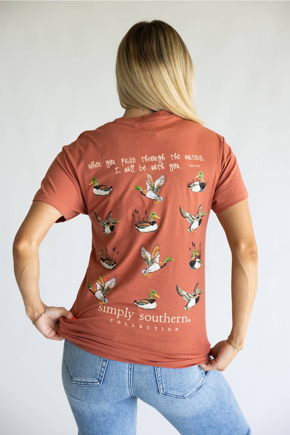 A terracotta-colored short-sleeve t-shirt shown from the back, featuring a graphic print of multiple flying mallards with handwritten-style text above and below. The brand 'simply southern.