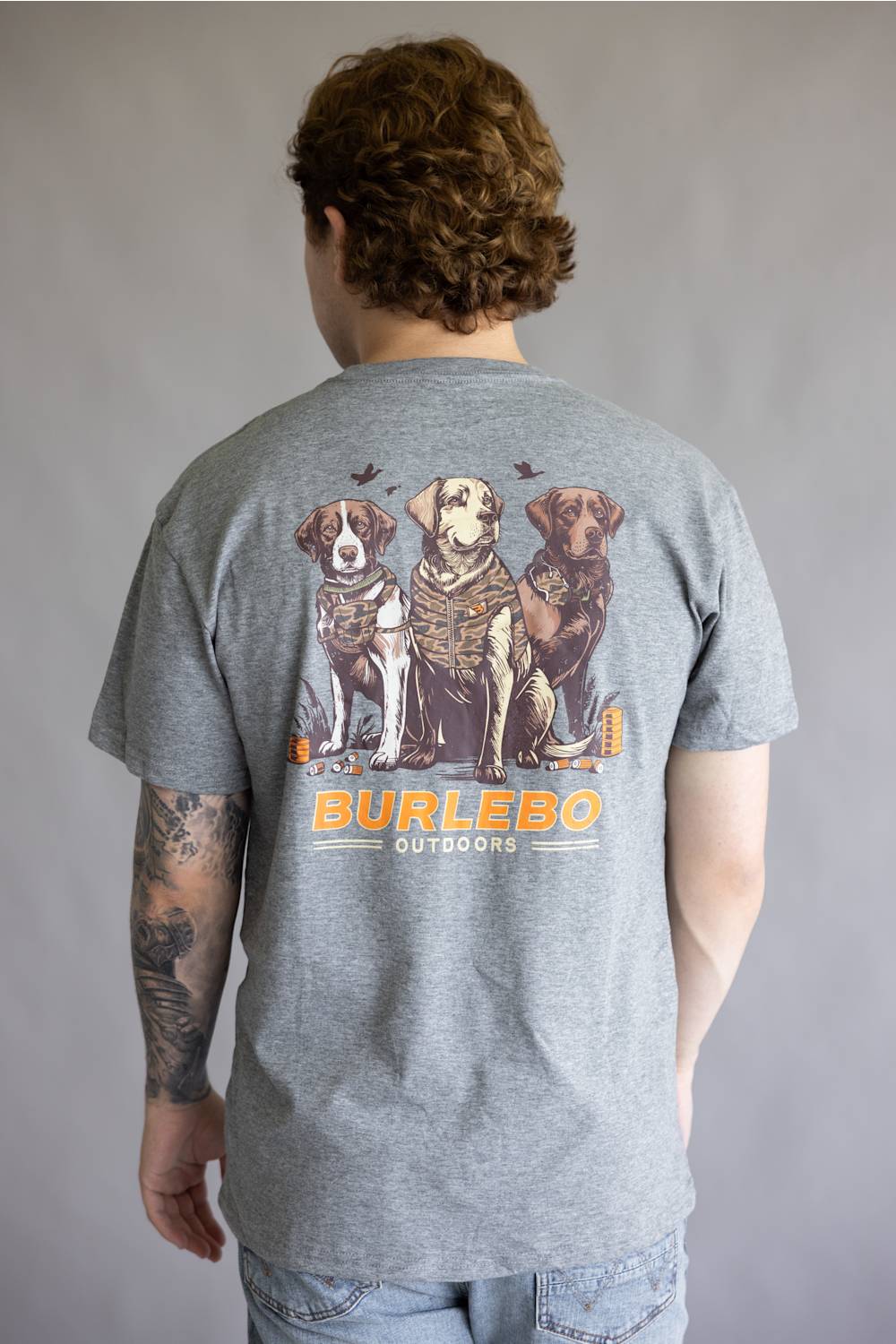 A man viewed from behind wearing a heather gray t-shirt with a large graphic print of three dogs and the text 'BURLEBO OUTDOORS' on the back.