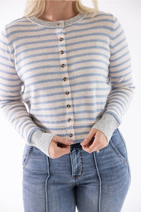 A woman wearing a cream and light blue striped cardigan sweater with brown buttons, paired with blue jeans, shown from the neck down against a white background.