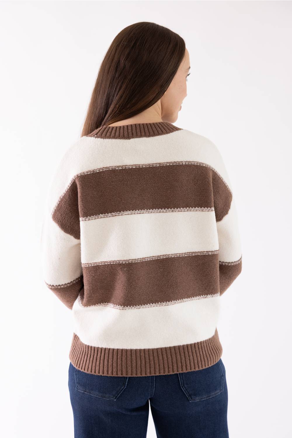 A woman viewed from the back wearing a cream and brown horizontally striped knit sweater with ribbed collar, cuffs, and hem, paired with dark blue jeans against a plain white studio background.