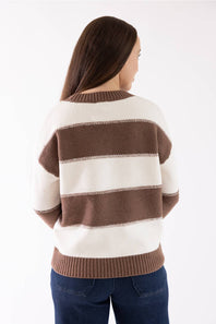 A woman viewed from the back wearing a cream and brown horizontally striped knit sweater with ribbed collar, cuffs, and hem, paired with dark blue jeans against a plain white studio background.