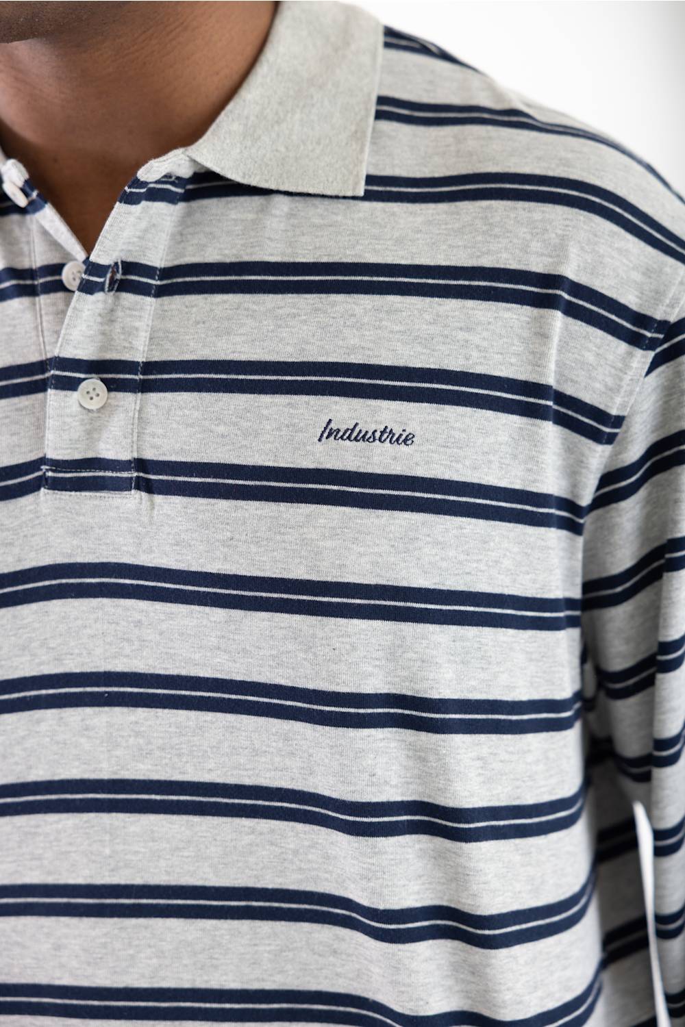 Close-up of a man wearing a heather gray polo shirt with navy blue horizontal stripes and a small embroidered 'Industrie' logo on the chest.