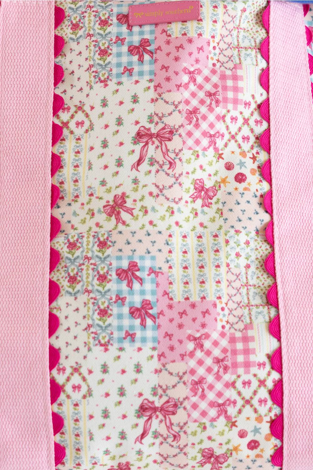 A close-up of a pink and white bag, featuring various floral, gingham, and bow patterns with pink ribbon motifs, bordered by pink satin-like trim.