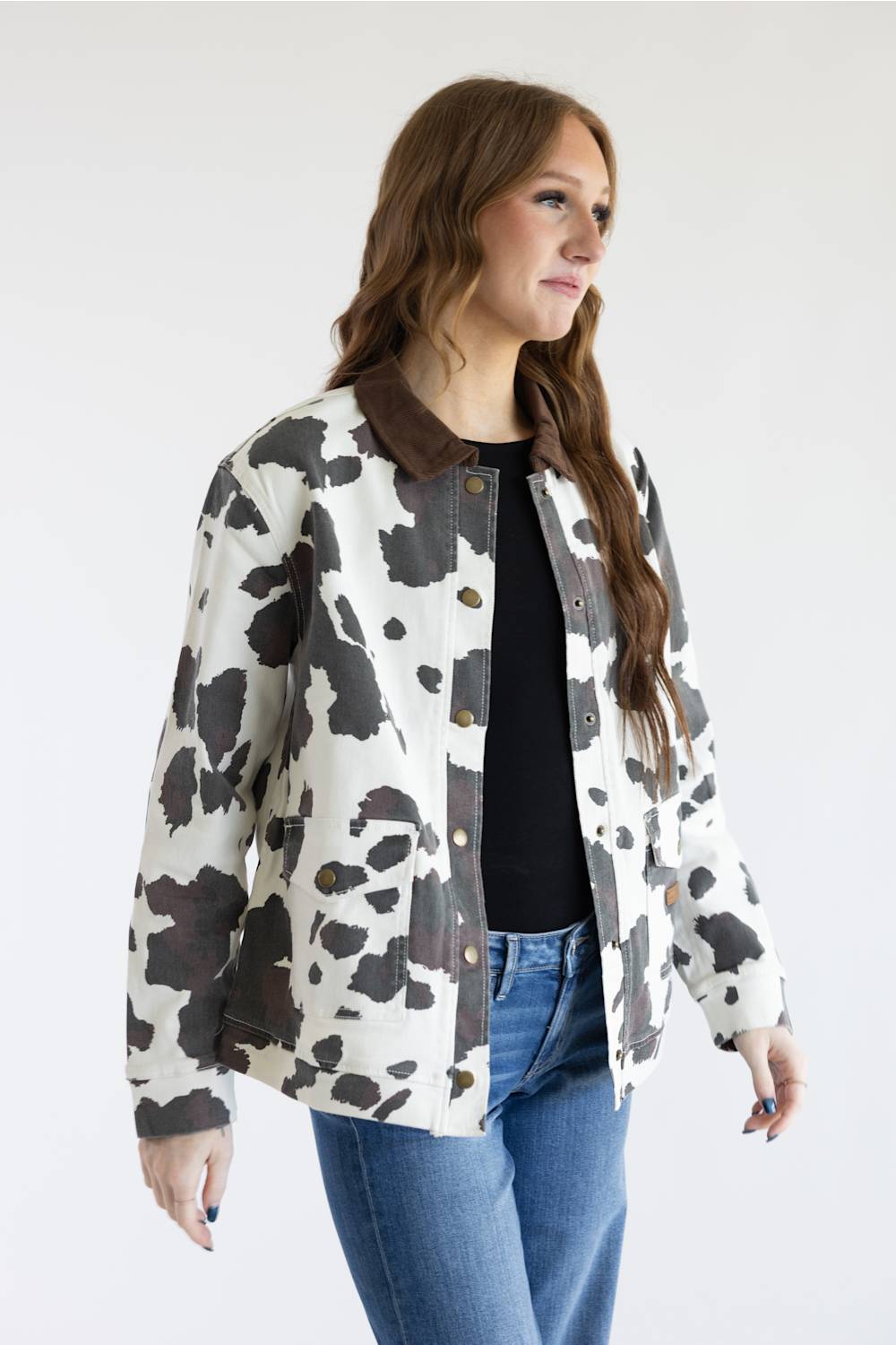 A woman wearing a cow-print jacket with a brown collar, styled with a black top and blue jeans against a plain white studio background.