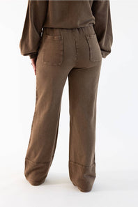 A person shown from the back wearing loose brown wide-leg pants with a matching brown top, photographed against a clean white studio background.