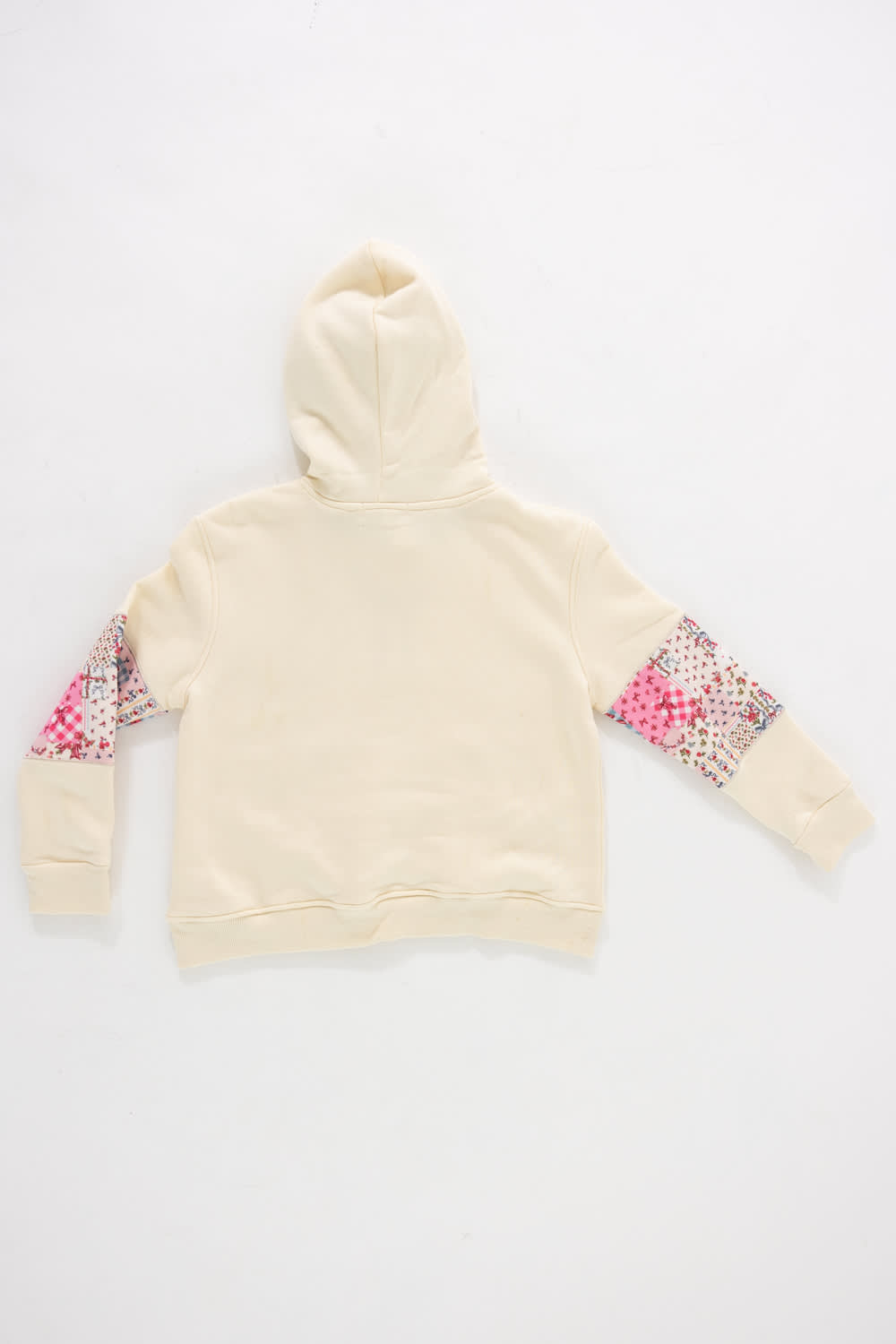 Back view of a girls' cream-colored pullover hoodie featuring pink patchwork floral elbow patches and an attached cream hood against a plain white background.