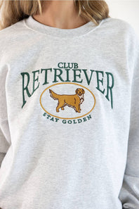 Close-up shot of the Sweet Claire Club Retriever Sweatshirt in Ash heather grey, highlighting the green arched "CLUB RETRIEVER" text, yellow oval frame with an embroidered golden retriever, and green "STAY GOLDEN" lettering.