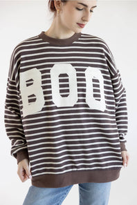 A woman posing in a brown and white horizontally striped sweatshirt with a large white BOO graphic on the front, paired with light blue jeans, against a plain white background.