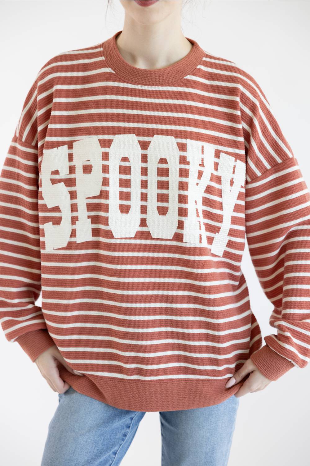 Women wearing dusty mauve sweatshirt with white horizontal stripes, SPOOKY screen printed on front and blue denim jeans on a basic background