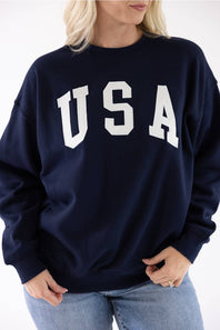 Close-up of a navy blue Reflex crewneck sweatshirt featuring large white "USA" block lettering across the chest.