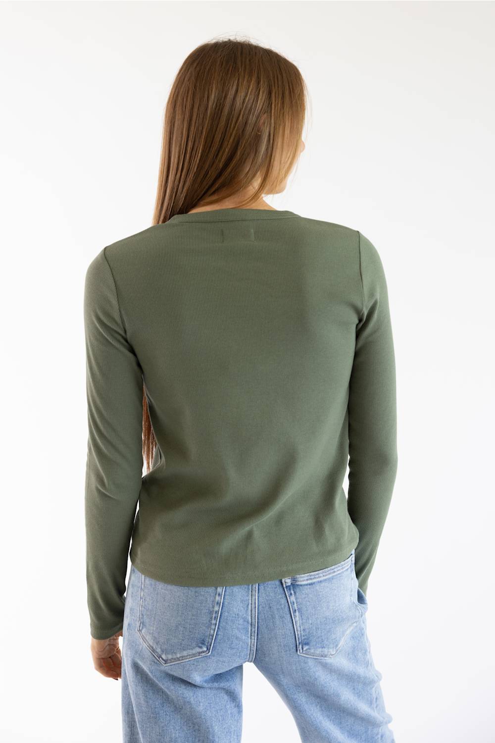 A woman viewed from behind wearing a fitted long-sleeve crewneck top in olive green and light blue jeans, against a plain white studio background.