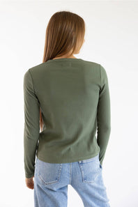 A woman viewed from behind wearing a fitted long-sleeve crewneck top in olive green and light blue jeans, against a plain white studio background.