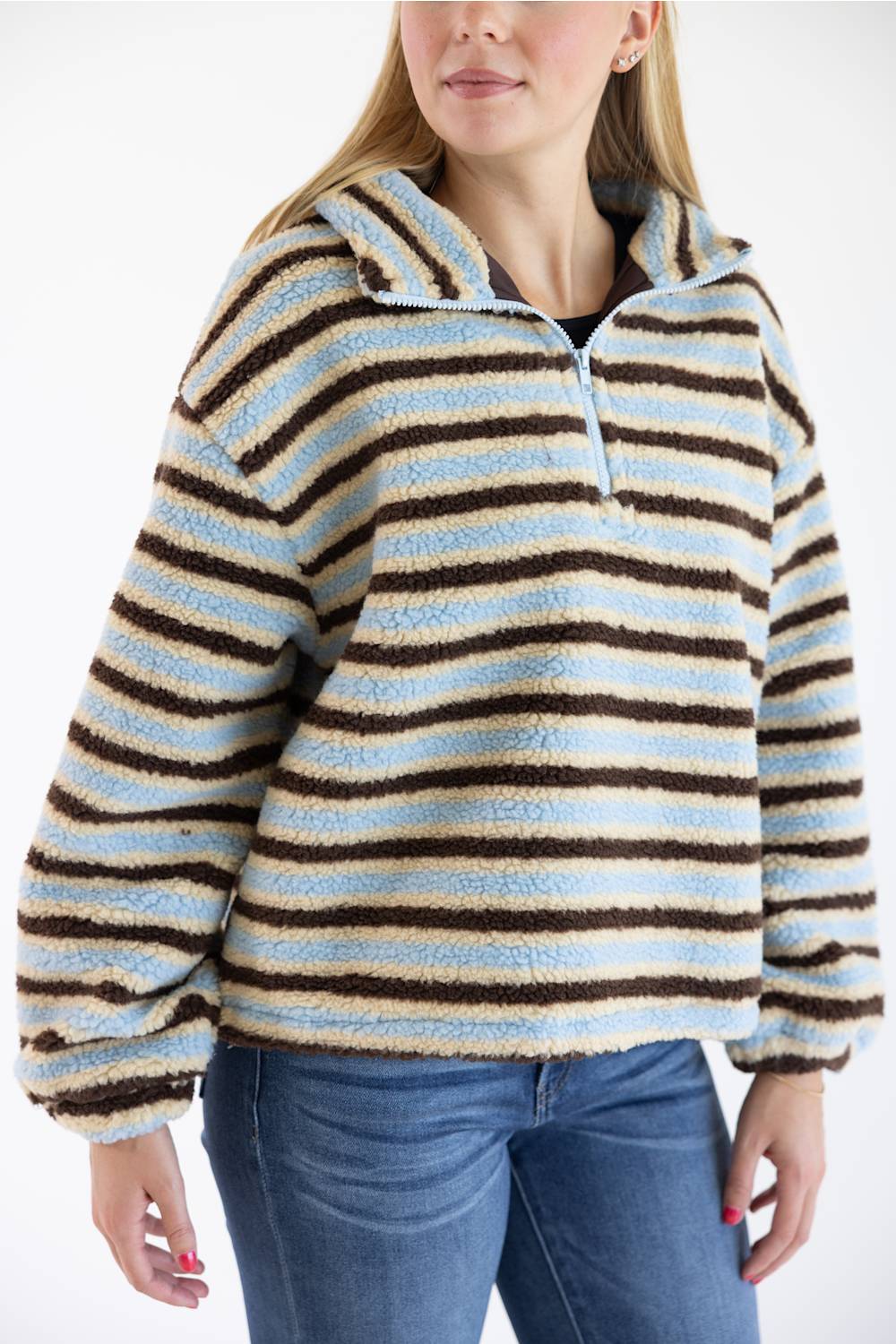 A woman wearing a fuzzy quarter-zip fleece pullover with horizontal stripes in light blue, cream, and dark brown, paired with blue jeans against a plain white background.