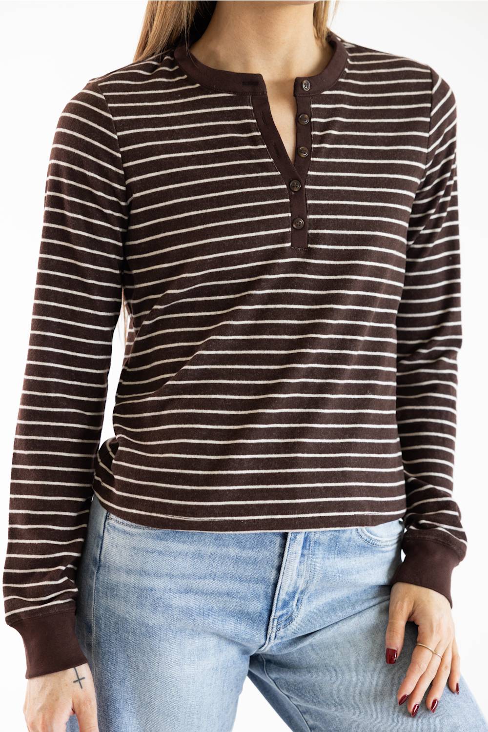 A woman wearing a brown and beige horizontally striped long-sleeve henley shirt with a button placket, paired with light blue jeans.