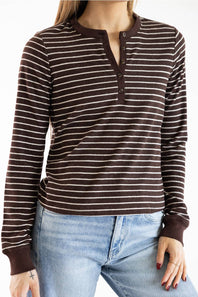 A woman wearing a brown and beige horizontally striped long-sleeve henley shirt with a button placket, paired with light blue jeans.
