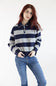 A woman with red hair wearing a navy and gray horizontally striped long-sleeve polo sweater and blue jeans, standing against a plain white studio background.