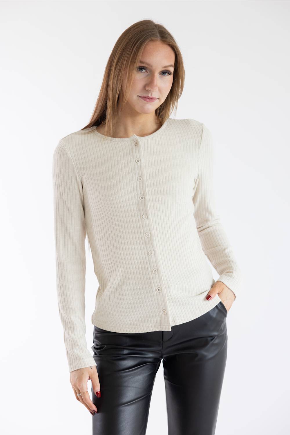 A woman modeling a cream ribbed knit long-sleeve cardigan with a button front, paired with black faux-leather pants, against a plain white studio background.