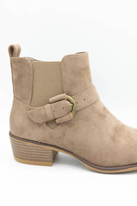 A beige suede ankle boot with a matching elastic side strap and a gold-tone buckle, shown from a side profile on a white background.