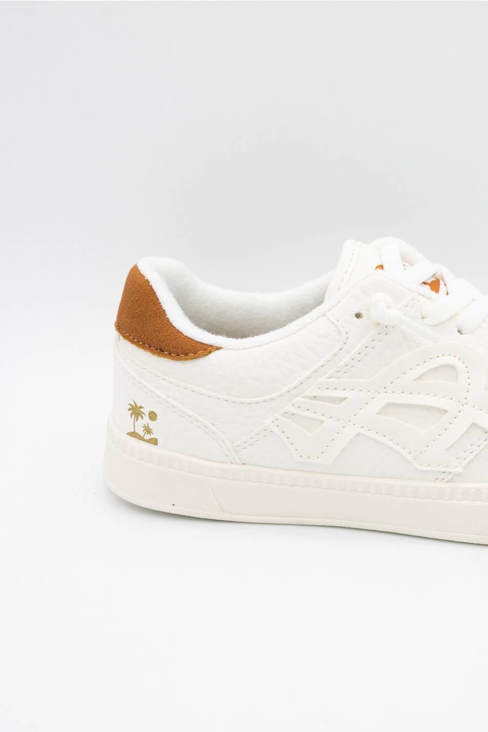 A close-up side view of a white low-top sneaker with a brown heel tab and a small gold palm tree logo on the side, set against a plain white background.