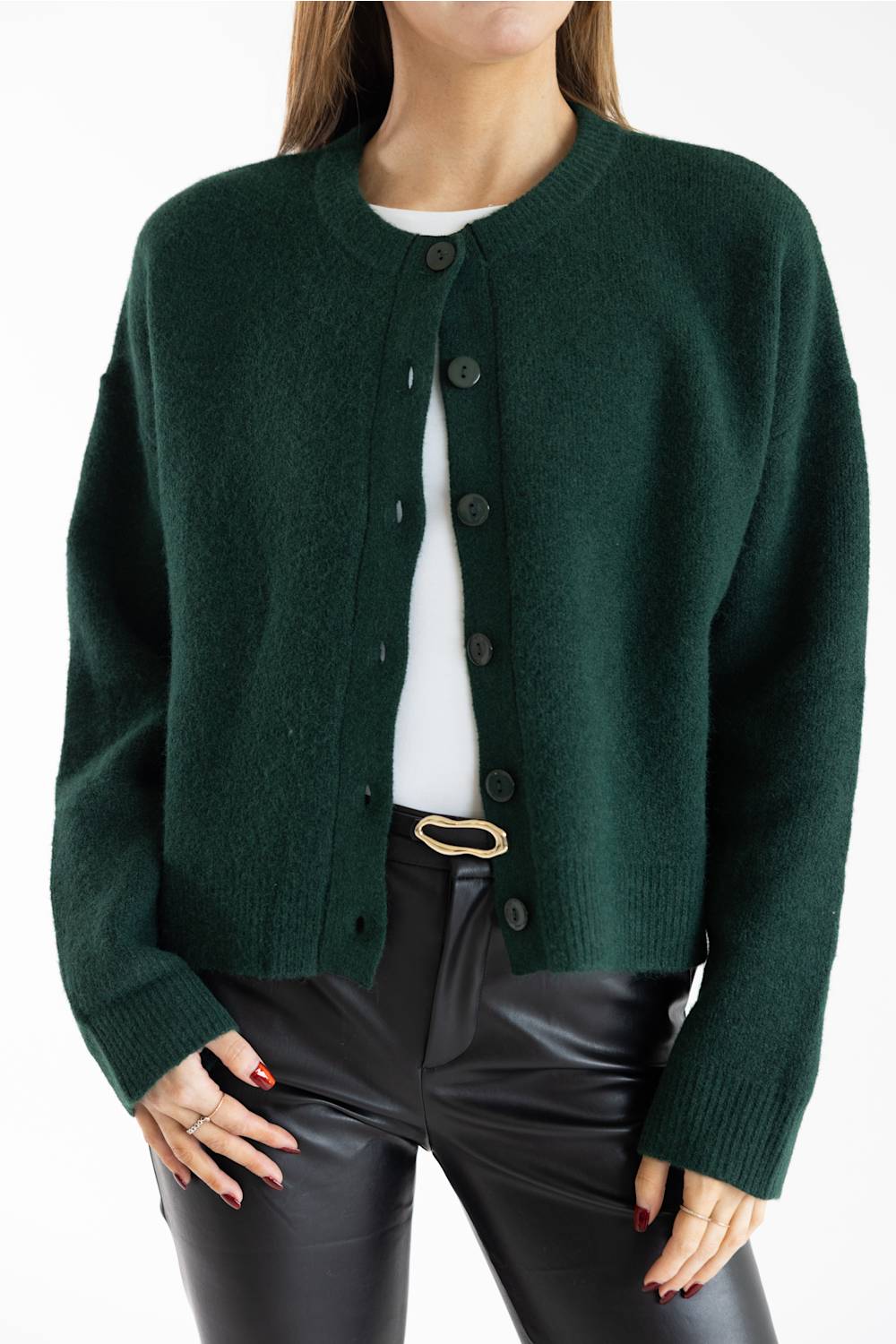A woman wearing a dark forest green knit cardigan with a crew neck and dark buttons, layered over a white top and paired with black pants.