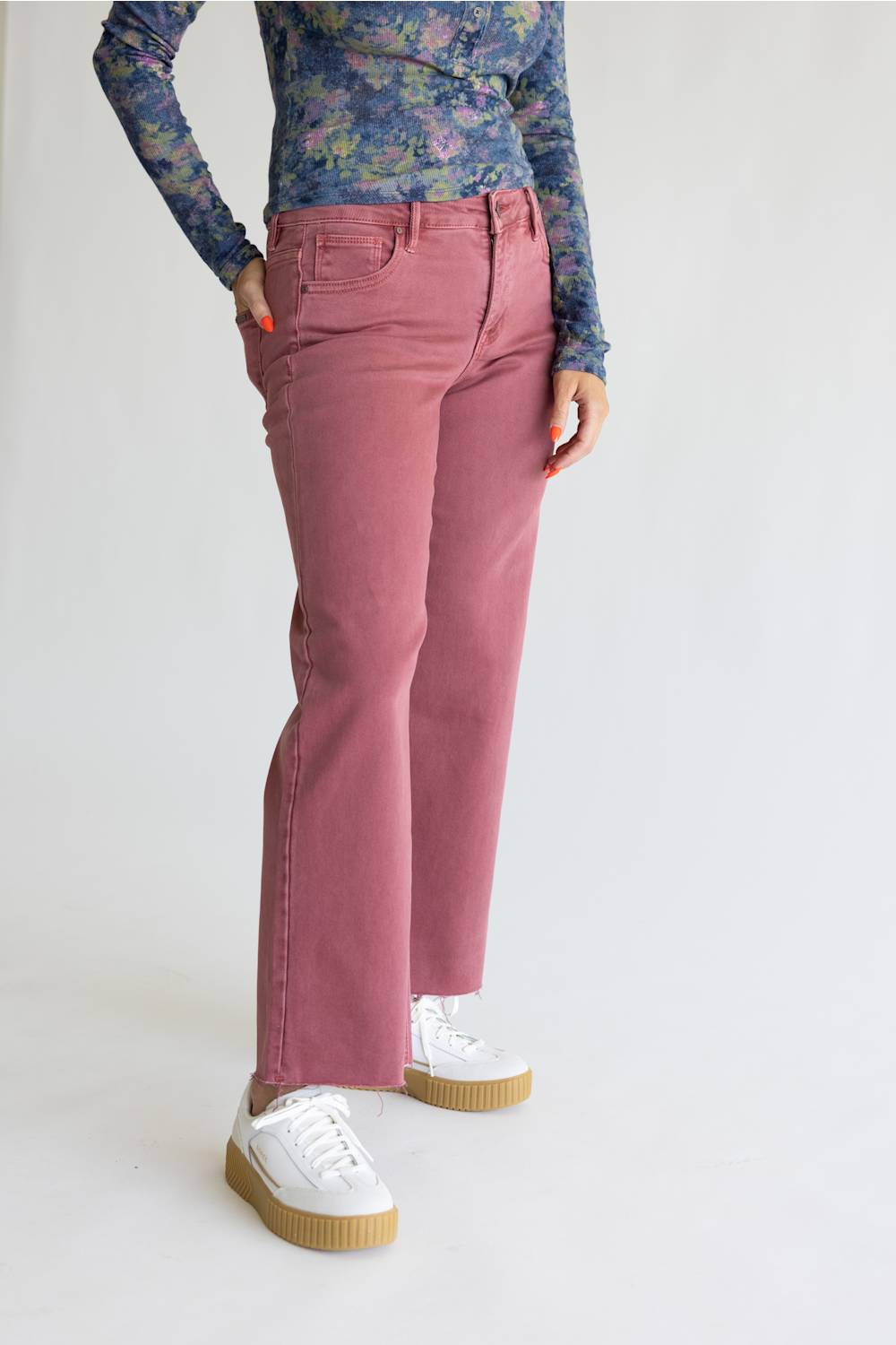 A model wearing dusty rose pink wide-leg jeans, a blue floral long-sleeve top, and white platform sneakers, standing against a plain white studio background.