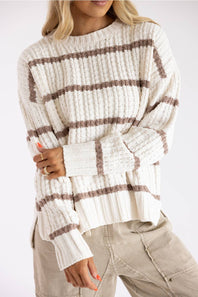 Close-up view of a model wearing a Paper Cut Clothing / Pink Rose white and tan striped crewneck tunic sweater with side slits, paired with beige utility pants against a plain backdrop.
