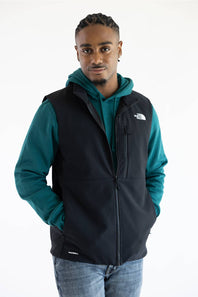 A person wearing a black vest over a teal hoodie, with The North Face logo printed in white on the upper right chest.