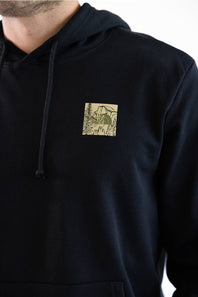 A close up of a person wearing a black pullover hoodie with a tan graphic featuring The North Face logo with Half Dome behind it.
