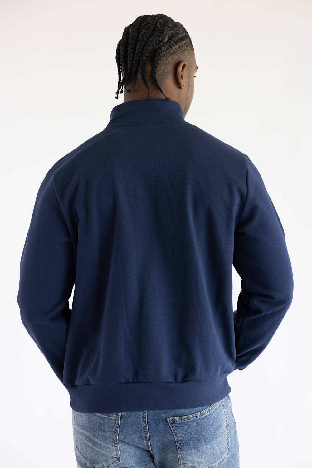 A man viewed from behind wearing a navy blue quarter-zip sweatshirt and blue jeans against a plain white studio background.