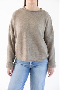 A woman wearing a light brown crewneck knit sweater and light blue jeans, shown from the mouth down against a plain white background.