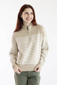 A smiling woman with red hair wearing a beige and white horizontally striped quarter-zip sweater and olive green pants, photographed against a plain white studio background.