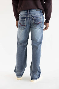 Rear view of a person wearing light-wash blue jeans with a dark brown sweatshirt and white sneakers against a plain white studio background.