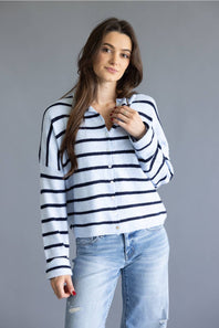 A woman modeling a white long-sleeve knit cardigan with navy blue horizontal stripes, paired with light-wash blue jeans, against a solid gray studio background.