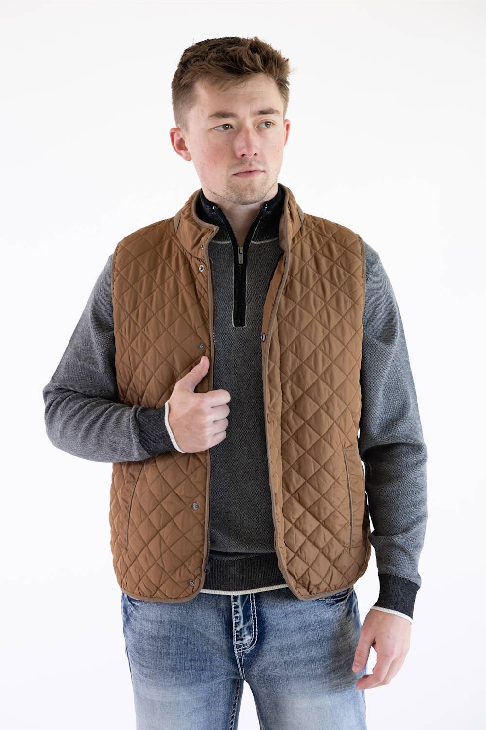 Man wearing a brown rhombus quilted field vest over a gray mock-neck pullover and jeans.
