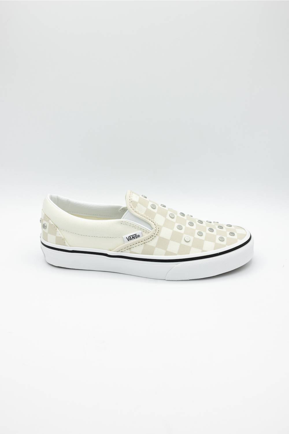 A single Vans slip-on platform sneaker in off-white and beige checkerboard canvas with metal studs on the toe, set against a plain white studio background.