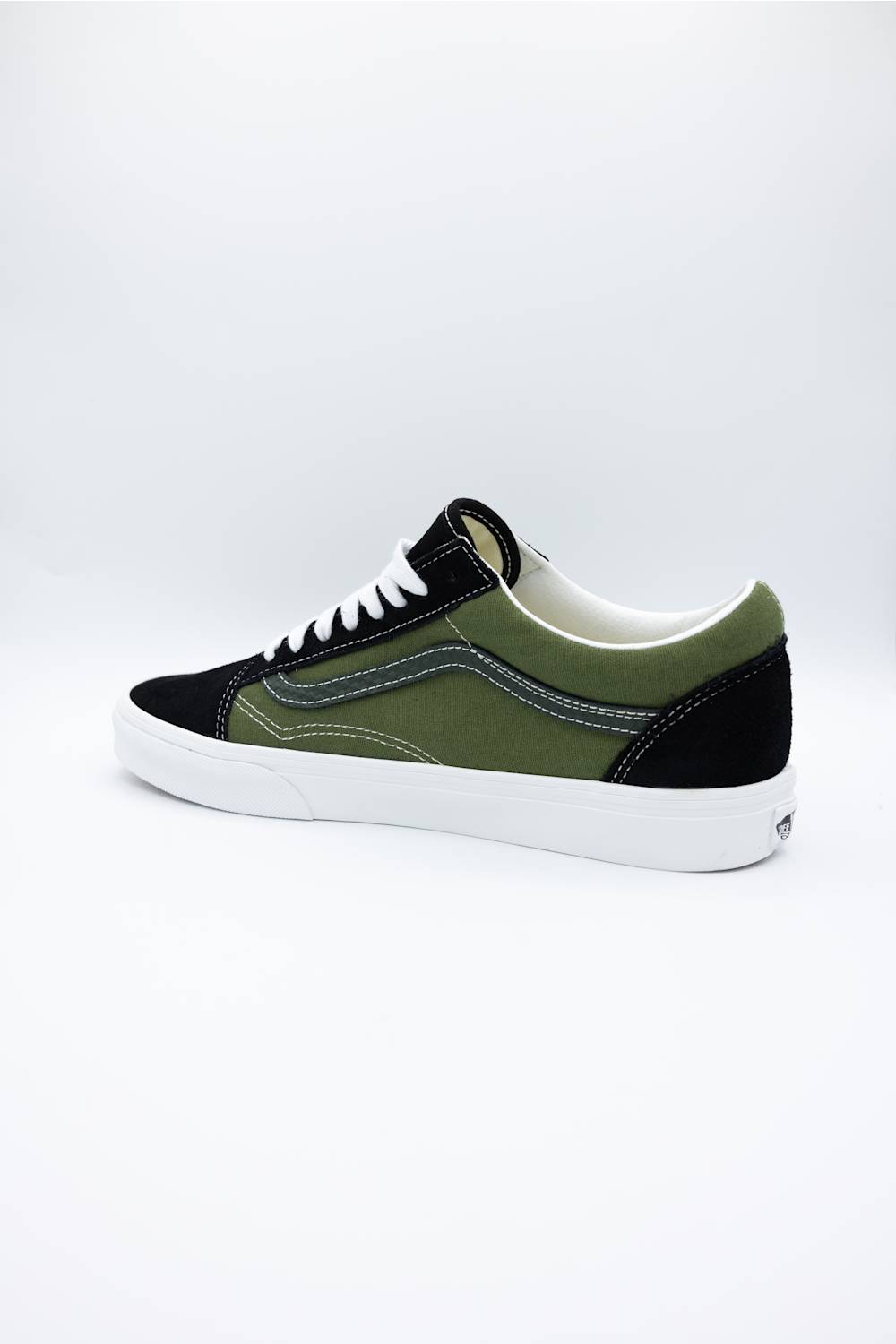 A low-top skate shoe in black and olive green suede with a white rubber sole, shown from a side profile view against a white studio background.